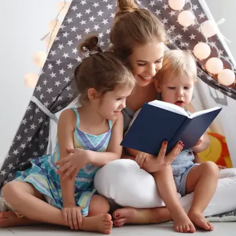 A parent and two young children reading together in a play tent